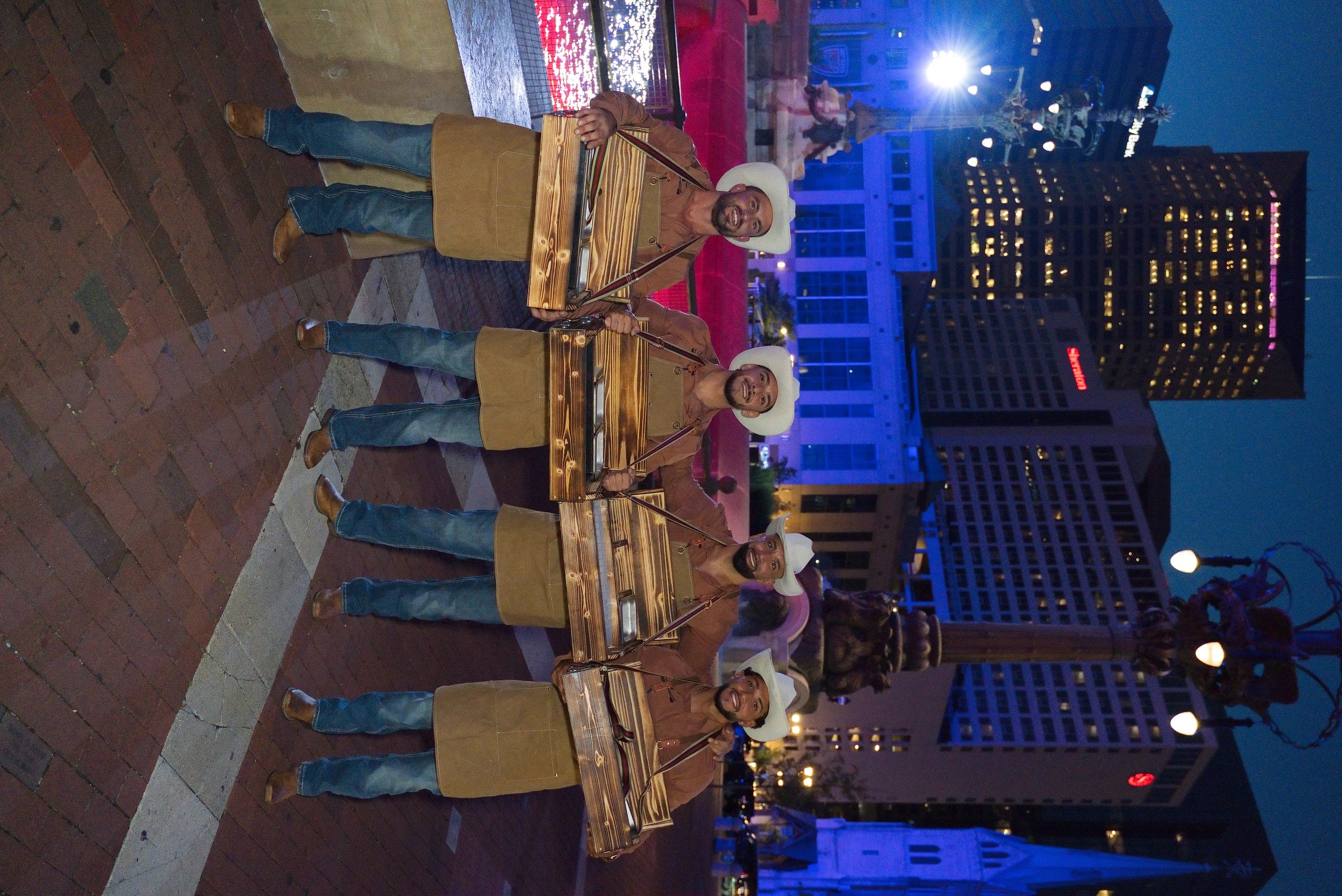 Four cowboys holding giant trays downtown at night